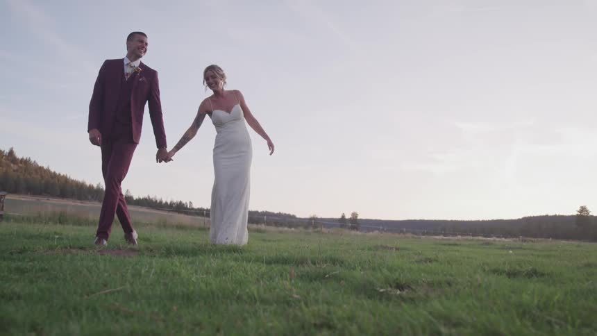 A bride and groom hold hands walking through an open pasture