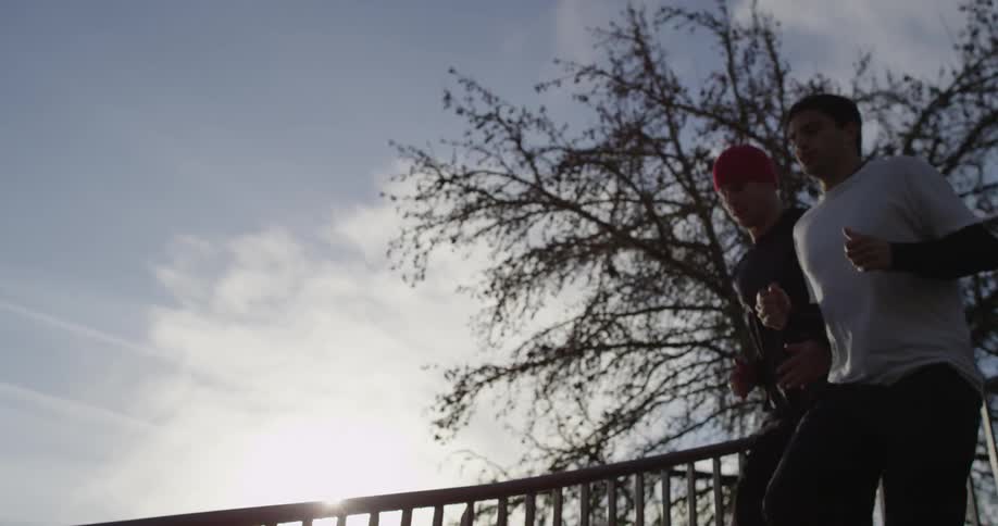 Two men jog down outdoor stairs on a sunny day