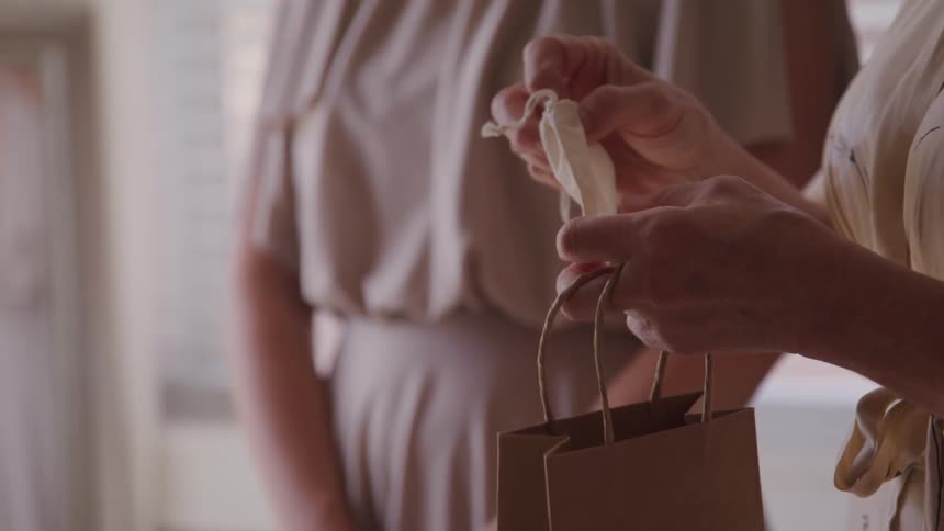 Two women stand together while one woman starts to open a bag that contains two rings