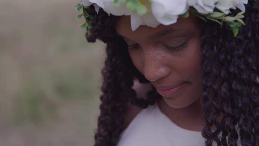 A woman stands and looks down with flowers around her head