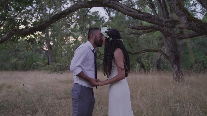 Bride and groom kissing under a large tree in the forest