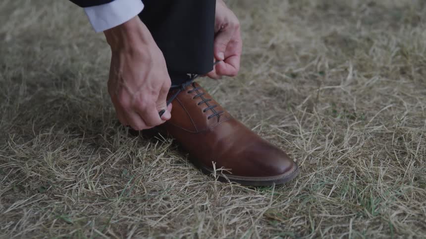 A person ties their shoes in the grass