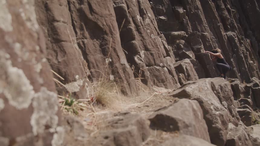 Woman climbs up the side of a mountain