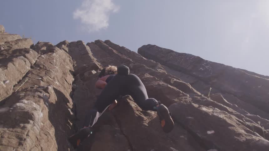 A female rock climber adjusts her footing as she ascends a tall rocky cliff side