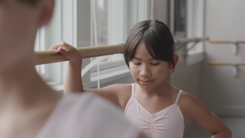 Young ballerinas perform exercises against the bar in sunny dance studio