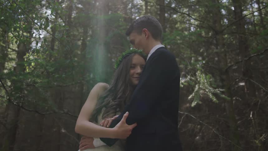 A man and woman wearing formal clothing hug in the woods