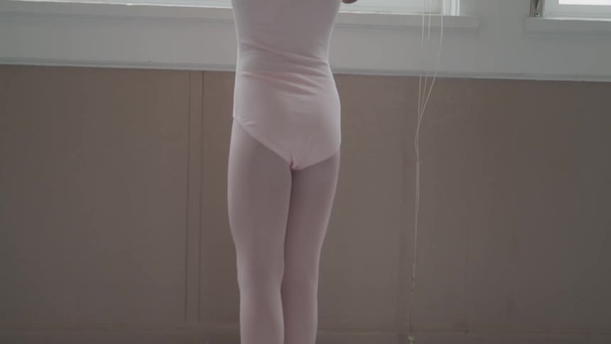 A young ballet dancer holds onto a bar and looks out the window