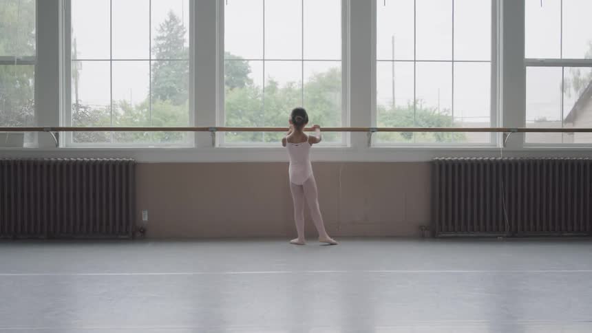 Little ballerina holding handrail warms up for dancing in the ballet studio