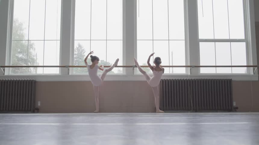 Two little ballerinas holding handrail warm up in the ballet studio