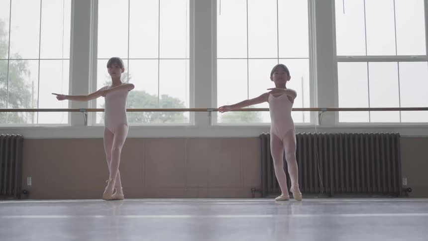 Two girl ballerinas jumping and spinning in a dance studio
