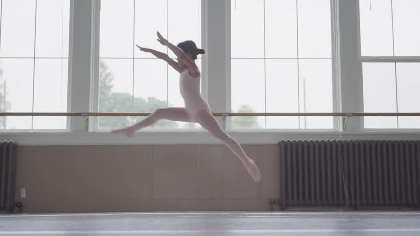Ballerina leaps before windows