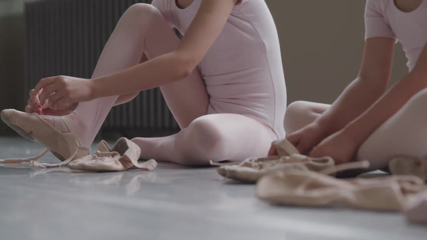 Two girls are putting ballet shoes on