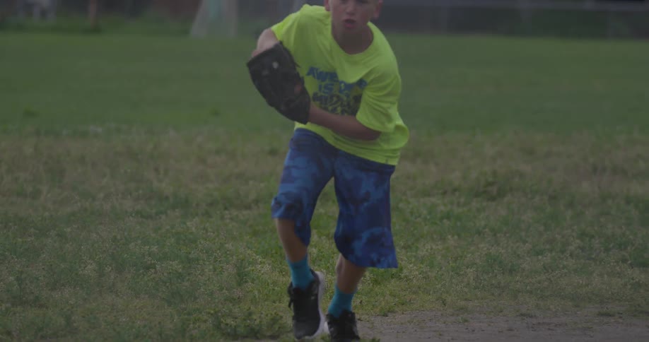 A boy runs on a field and catches a baseball before throwing it back
