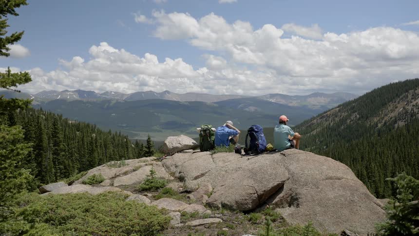 A man and woman sit on the ledge of a cliff and look at the landscape