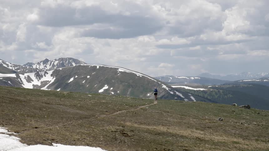 A person hikes through a field towards a snow covered mountain