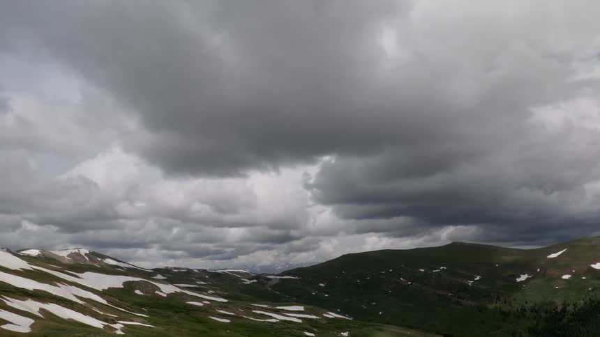 Clouds flow over snow dotted low mountains