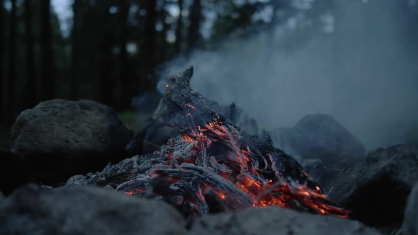 A campfire smolders with red hot ambers