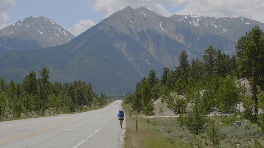 A person is hiking down the highway towards the mountains