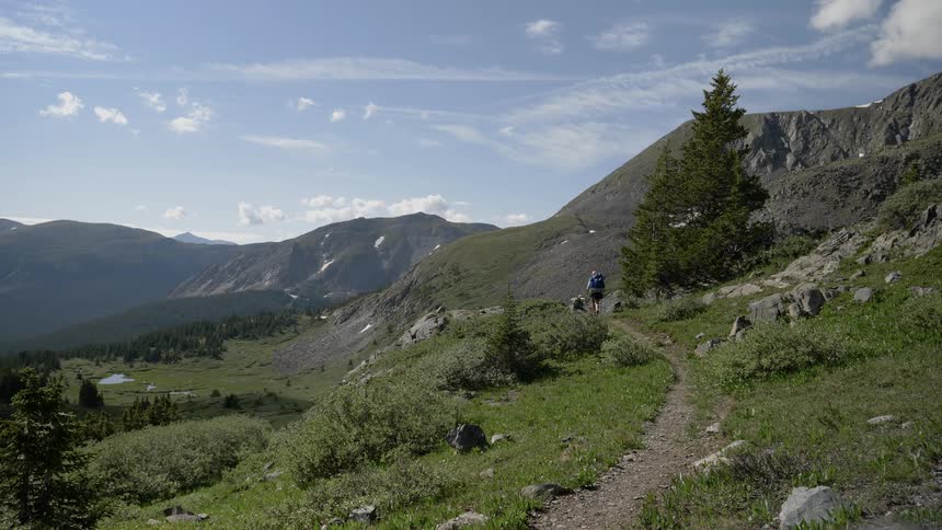 A pair of hikers walking down a narrow dirt trail in the mountains