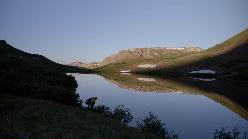 A person walks down a hills towards a lake