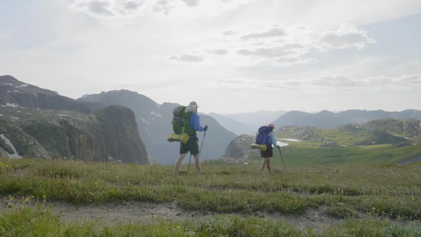 Backpackers hiking across a grassy meadow in the mountains