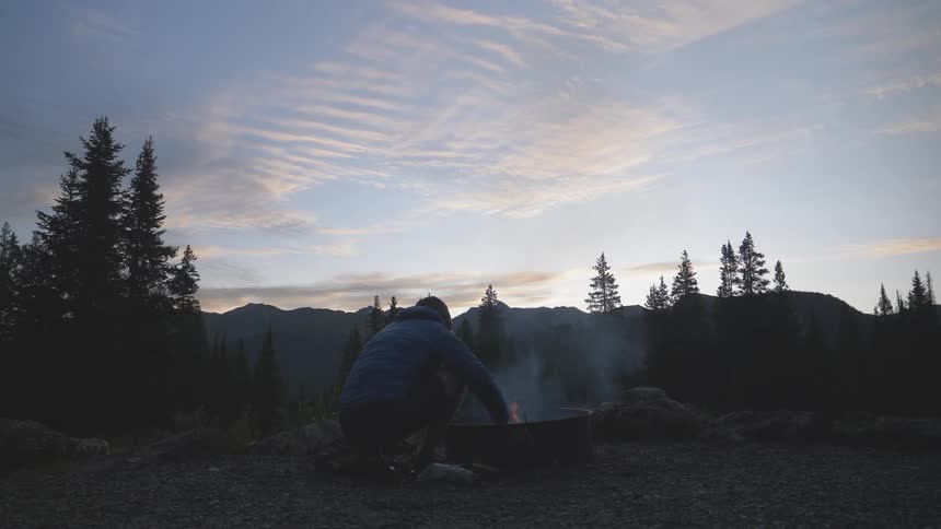 A man blows in a fire pit as he builds a fire