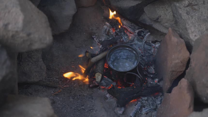 A pot sits on a burning campfire surrounded by rocks