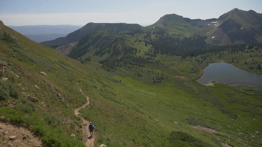 A man walks along a dirt path at the bottom of a slope
