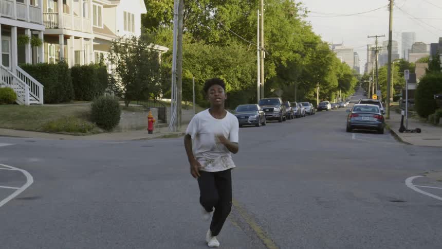 A adolescent black boy runs down the middle of the street