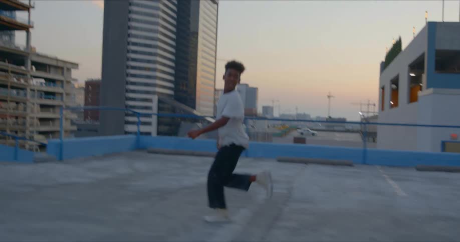 A young boy runs across a roof top and looks over the edge