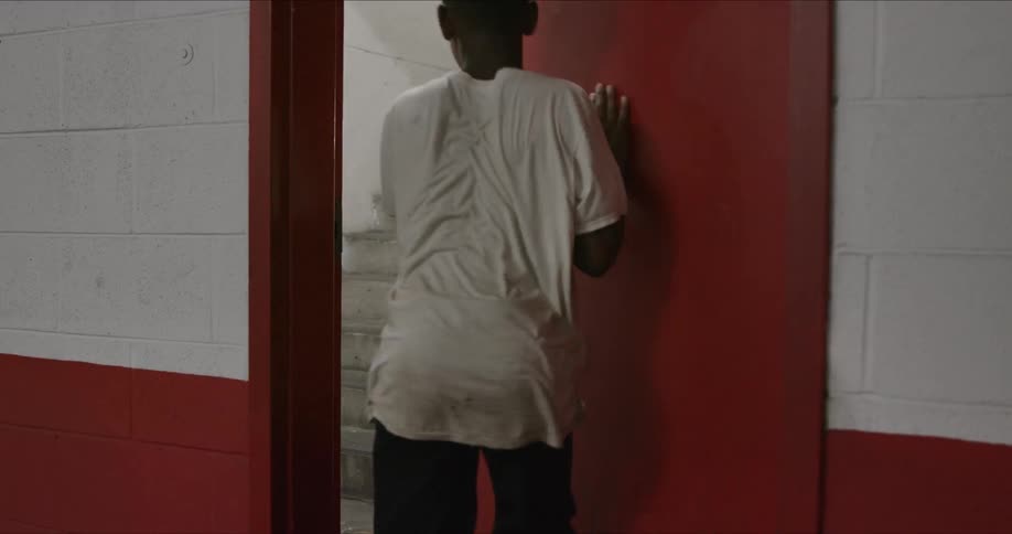 A young black male suddenly pushes open a red door and runs up the stairwell inside