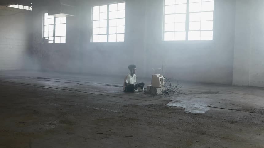 A person sitting in a large empty industrial space with a vintage crt monitor in front of them