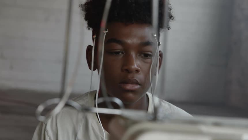 A black boy sitting before a monitor with electrodes on his head