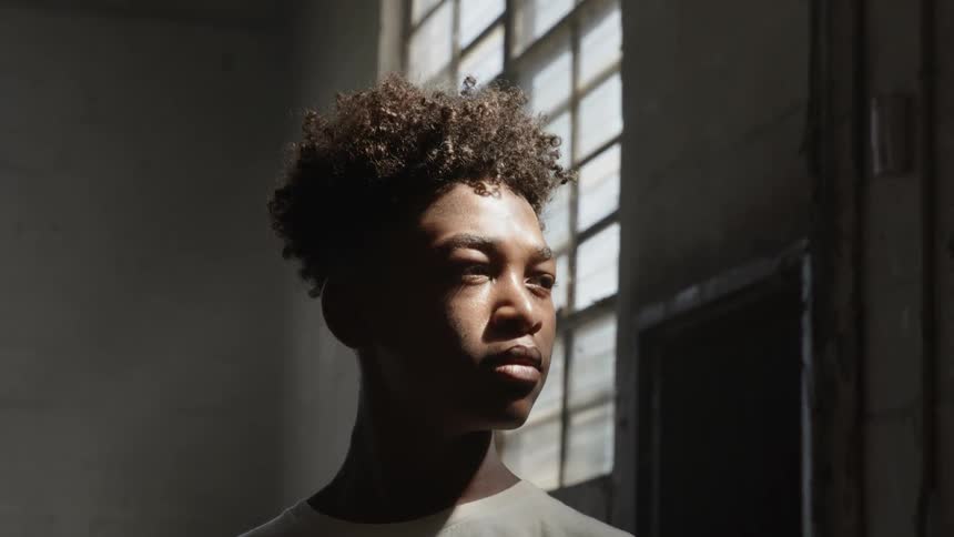 Black boy looks out the window and turns to the camera indoors