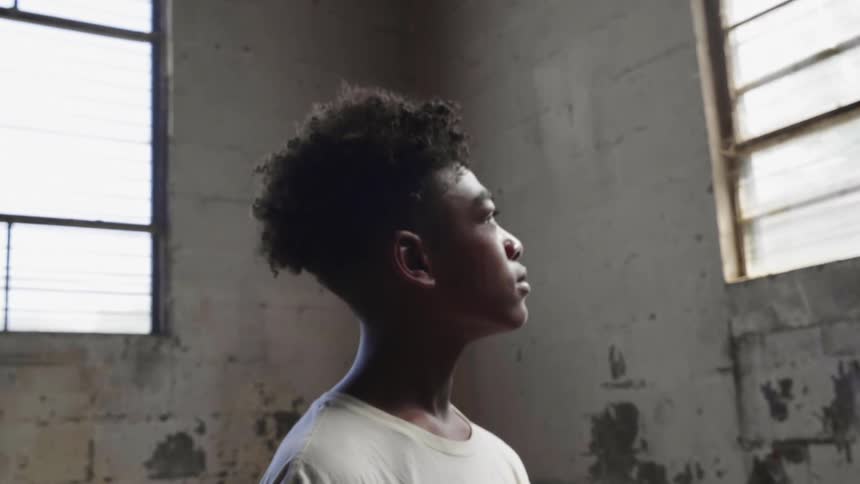 Black boy looks out the window in the worn building