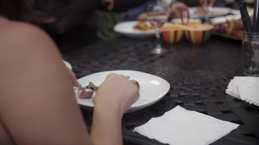 Woman sits at dinner with others, cutting her food