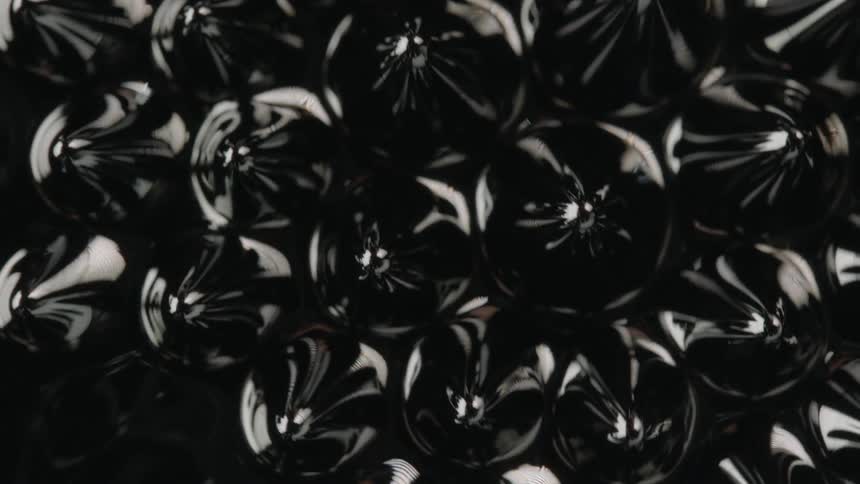 Black lumps raising to lift the surface of a black liquid before sinking back beneath and leaving the surface flat