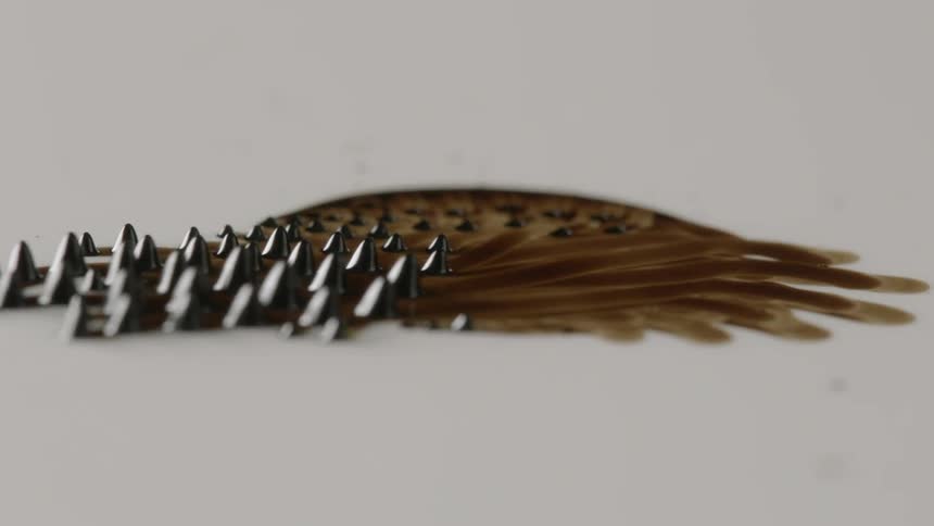 Ferrofluid moves on top of the surface of water leaving behind streaks as the lumps of ferrofluid move to the left