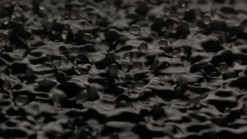 The surface of a dark liquid ripples violently as if the liquid is being vibrated from below