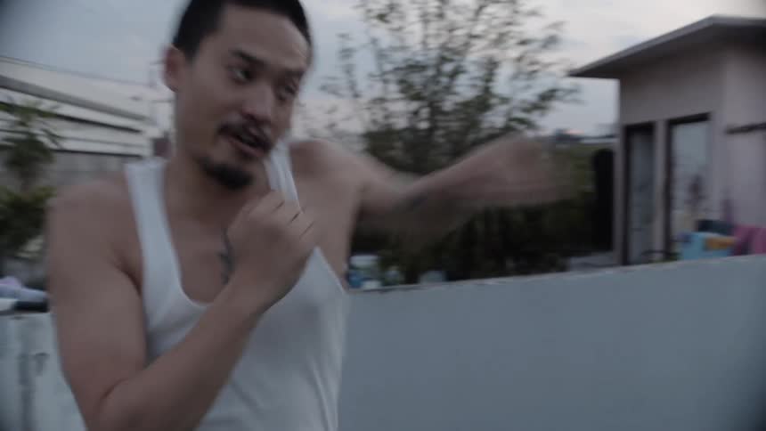 Man in a white shirt practices boxing jabs on an outdoor balcony
