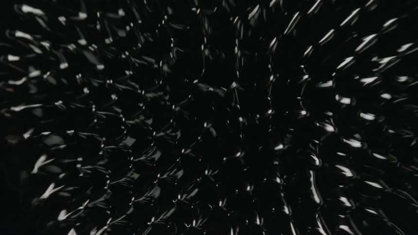 A multitude of spike emerge from the surface of a shiny black ferromagnetic fluid before they sink back into it