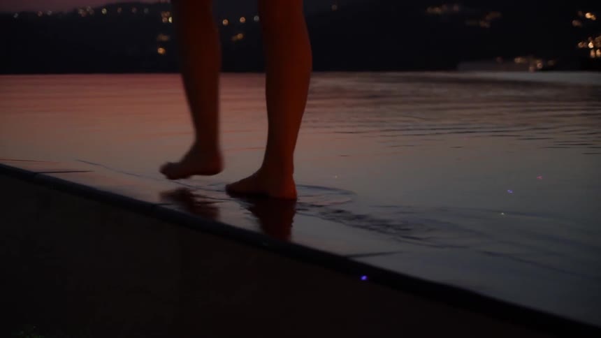 A person walking along the edge of a pool at night