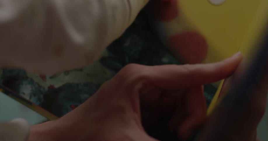 A close view of the hands of a woman and young child pointing at the pages in a book
