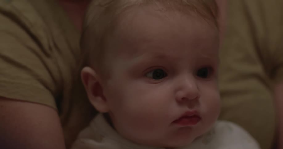 A baby watches the pages of a book being read to him