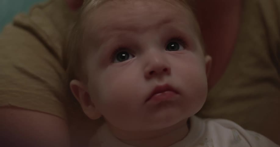 A baby is sitting in someone's lap looking up