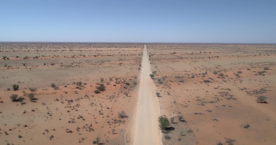 An long straight dust covered road runs through the middle of a wide open desert landscape