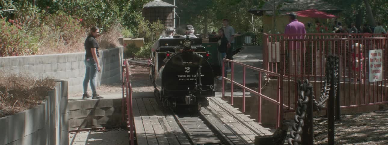 An pair of elderly men ride in a amusement park train ride as other patrons watch and await their turn