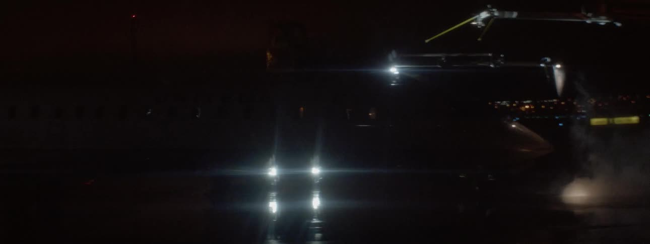 An airplane in an airport at night time being sprayed by a machine