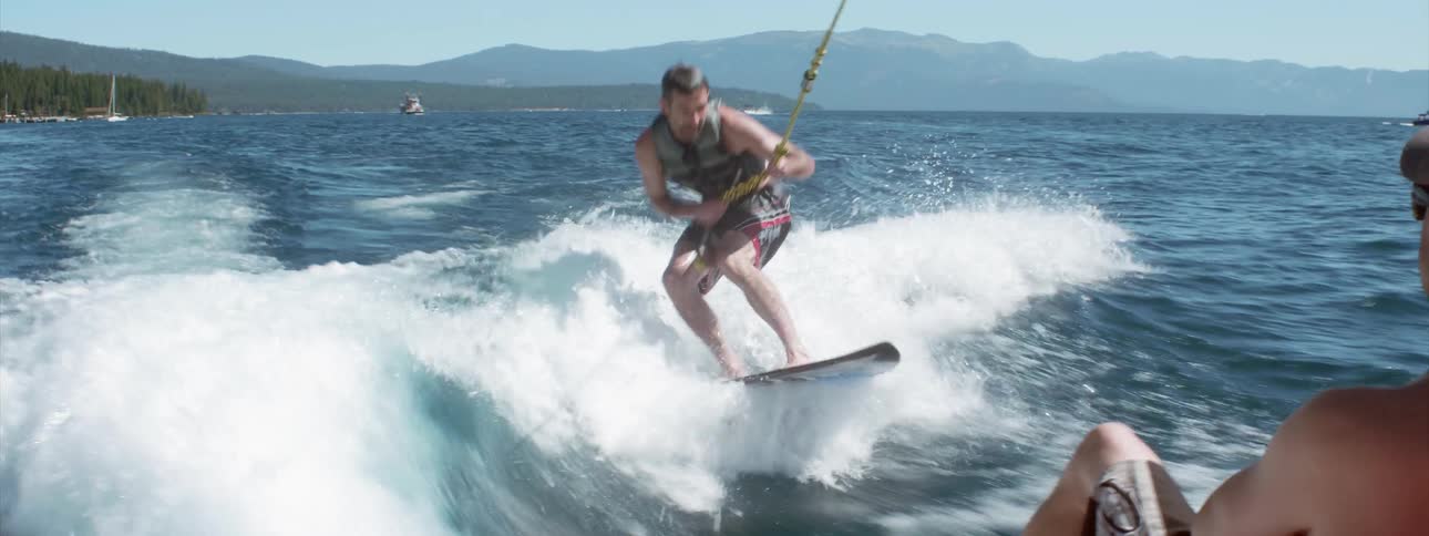 Friends in a boat cheer when a friend who is wake surfing falls off the board