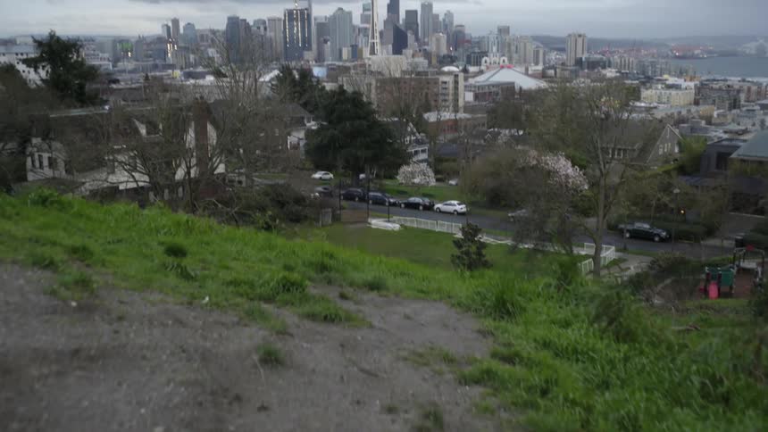 First person view of approaching the side of a grassy cliff and overlooking the seattle skyline on a cloudy day
